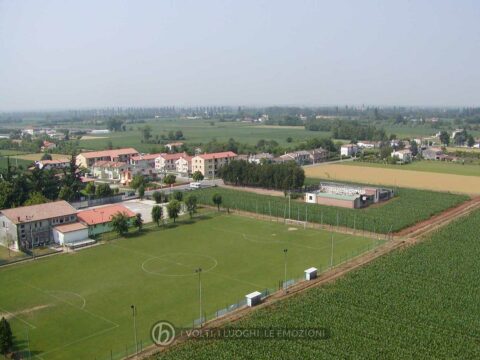 Foto Comune di Vedelago - 2006. In primo piano: il campo da calcio, l'edificio della scuola materna con attigua la nuova mensa. Più in là: il cimitero e di fronte la lottizzazione di via Massari. All'orizzonte si possono notare sulla sinistra gli alti cipressi di villa Emo e, sulla destra, il campanile di Fanzolo